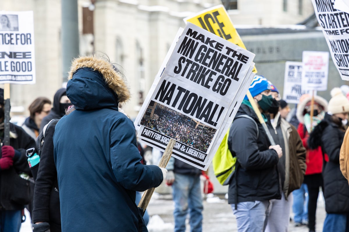 a protester holds a sign reading MAKE THE MN GENERAL STRIKE GO NATIONAL!
