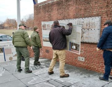 Four workers are using crowbars to remove signs from a brick wall