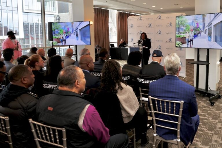 Desaree K. Jones speaking at a podium during a presentation of renderings.