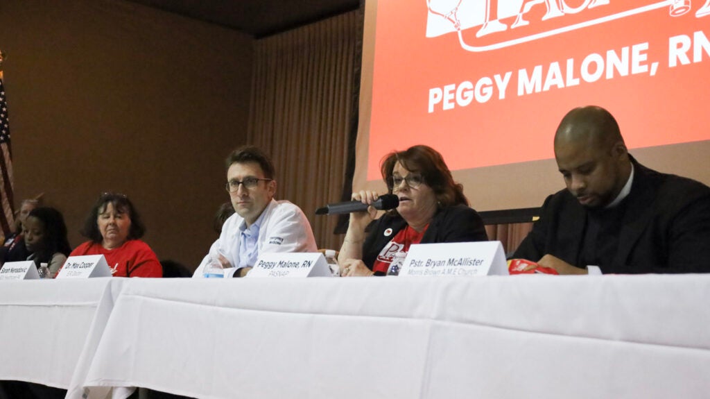 A panel of health care workers and a pastor sit at a table as part of a forum