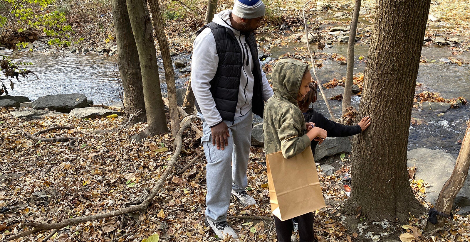An adult and two kids explore the outdoors near a creek