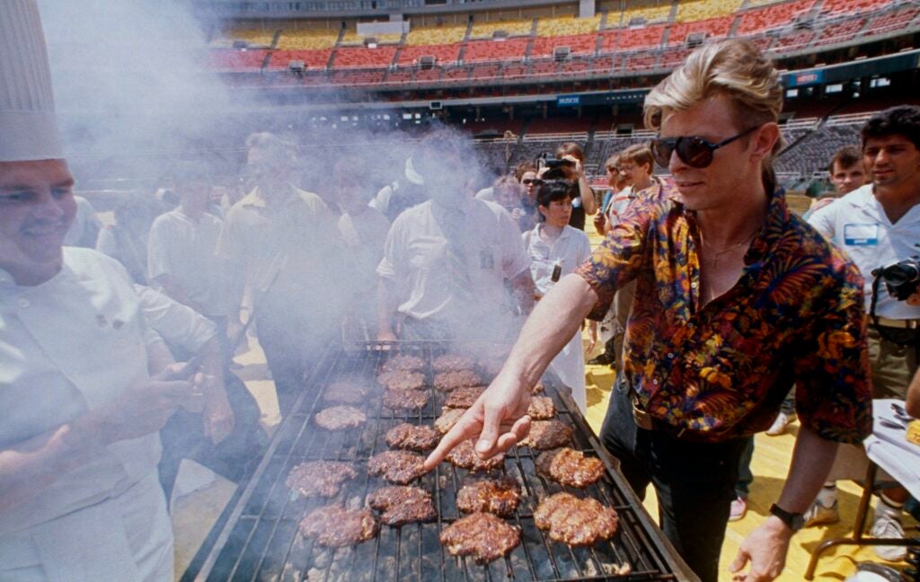 David Bowie flipping burgers on a big grill on the football field in the stadium