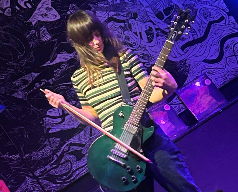 Emily Robb using a violin bow to play her guitar during a live performance
