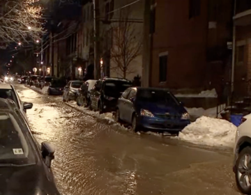A flooded street with cars parked on either side and snow on the ground