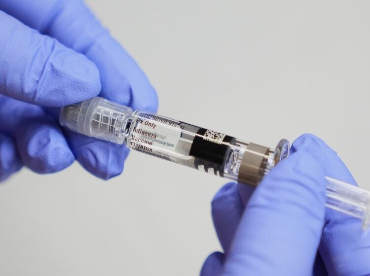 A certified medical assistant holds a syringe for a flu vaccine