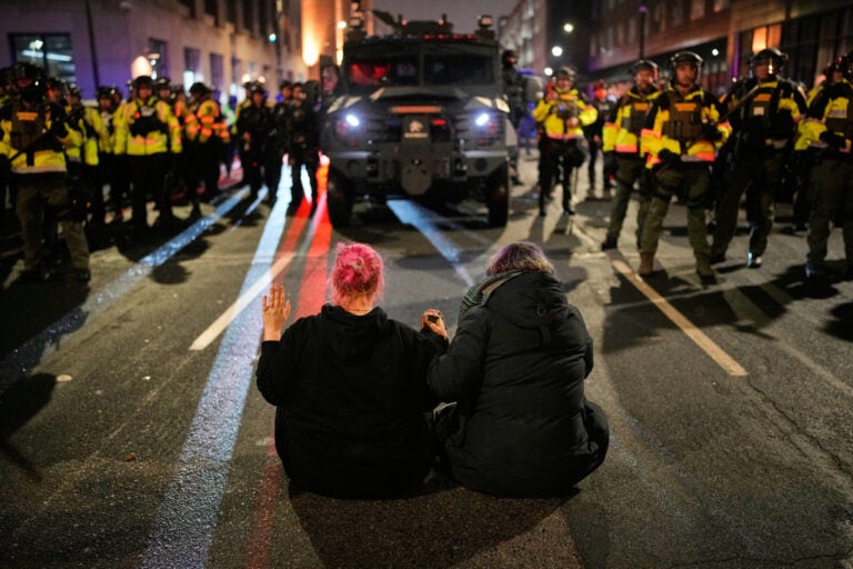 Two people sit in the street holding hands in front of Minnesota State Patrol during a protest
