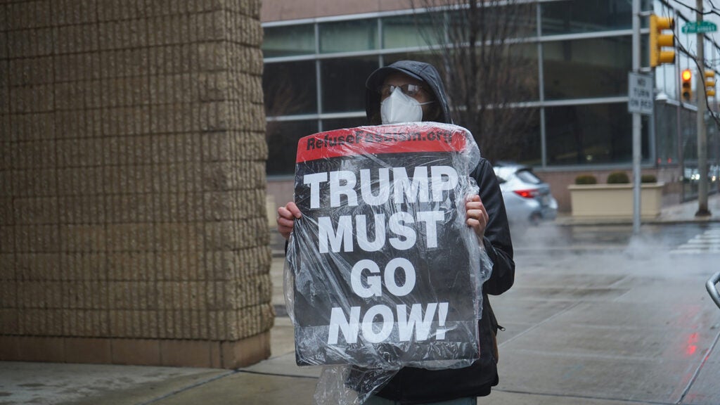 A protester holds a sign that reads "Trump Must Go Now!"