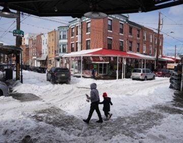 People cross a snow covered street in the aftermath of a winter storm in Philadelphia, Monday, Jan. 26, 2026.