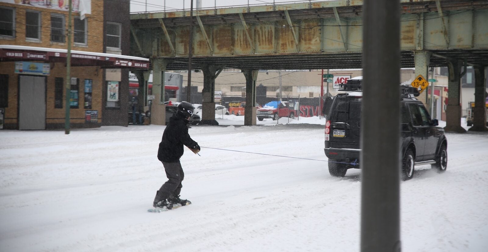 A snowboarder rides down Girard Avenue, connected to a car via rope, during a snowstorm in Philadelphia