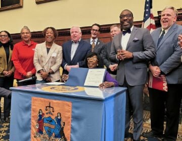 Cherelle Parker sitting at a table holding up the bill she just signed, surrounded by other officials