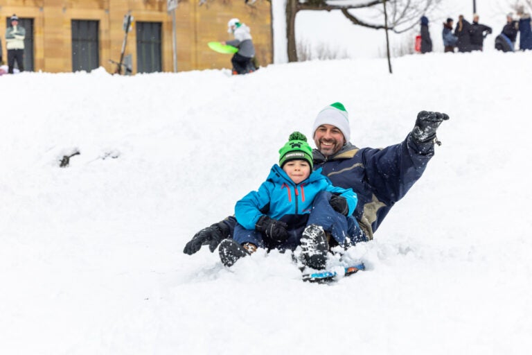 A man sledding down a hill at the Philadelphia Art Museum with a child after the snowstorm