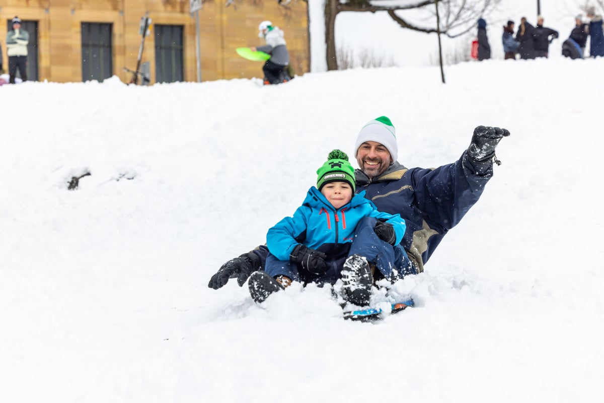 A man sledding down a hill at the Philadelphia Art Museum with a child after the snowstorm