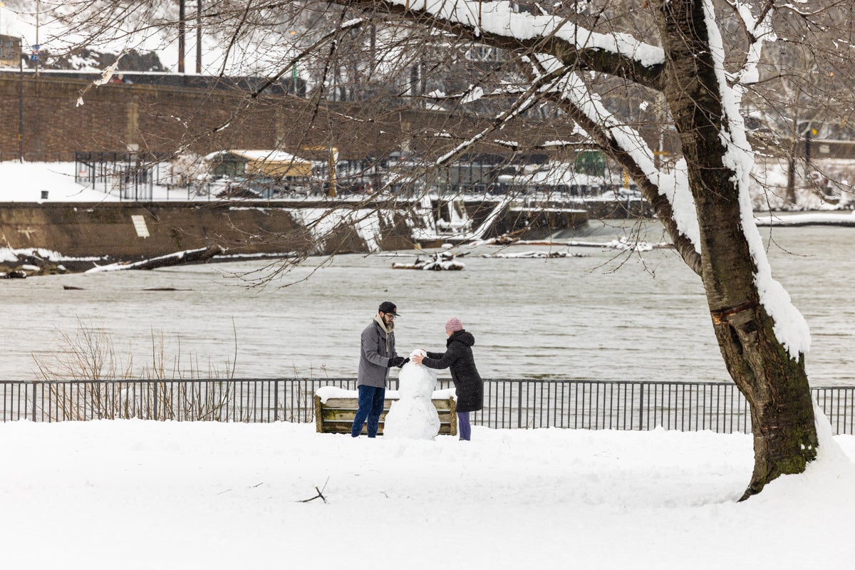 Two people build a snowman right alongside the Schuylkill River after the snowstorm