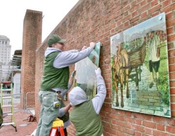 2025 02 19-e lee-philadelphia independence mall presidents house-slavery exhibit restored raising panel National Park Service employees restore the exhibit on slavery to the President's House Site on Independence Mall