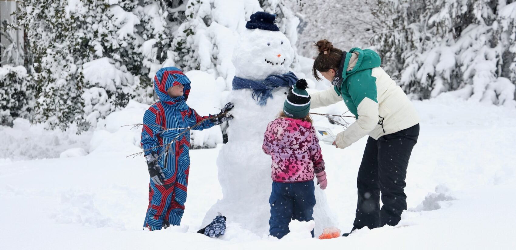 Leiloni Hanson building a snowman with her two children after a blizzard. They are tying a scarf around its neck in Moorestown, New Jersey