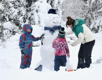 Leiloni Hanson building a snowman with her two children after a blizzard. They are tying a scarf around its neck