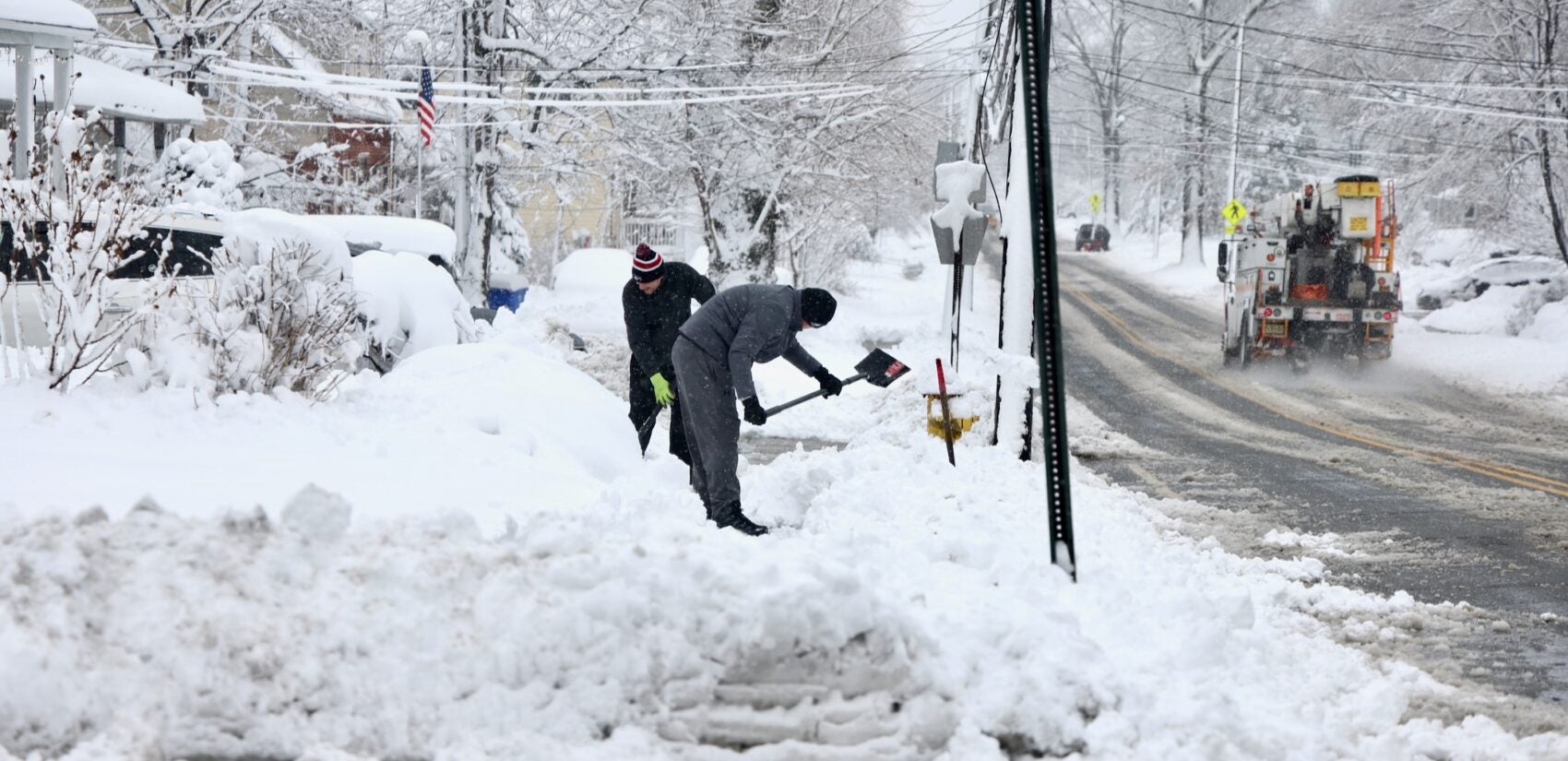Two people shoveling out driveways and sidewalks on a residential street after a huge snowstorm in Moorestown, New Jersey