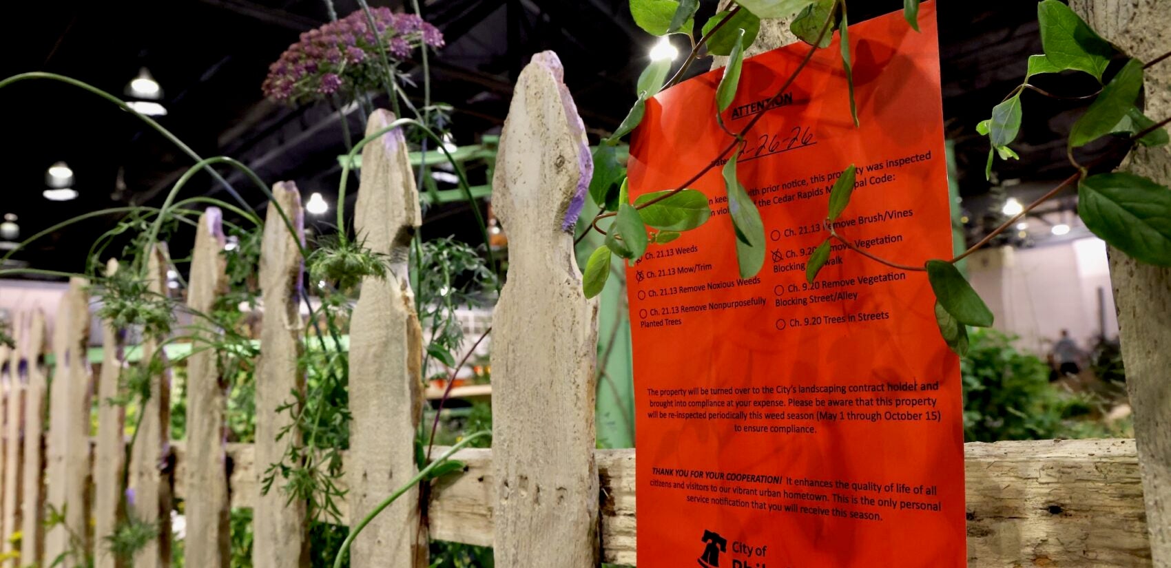 A notice ordering weeding, mowing and trimming is affixed to and overrun picket fence at the flower show
