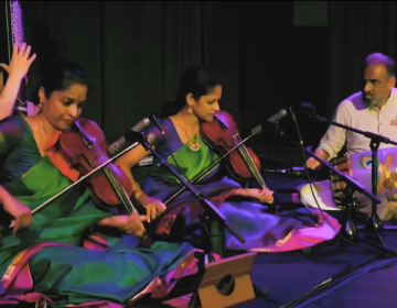 The Akkarai Sisters sitting on stage performing during a concert