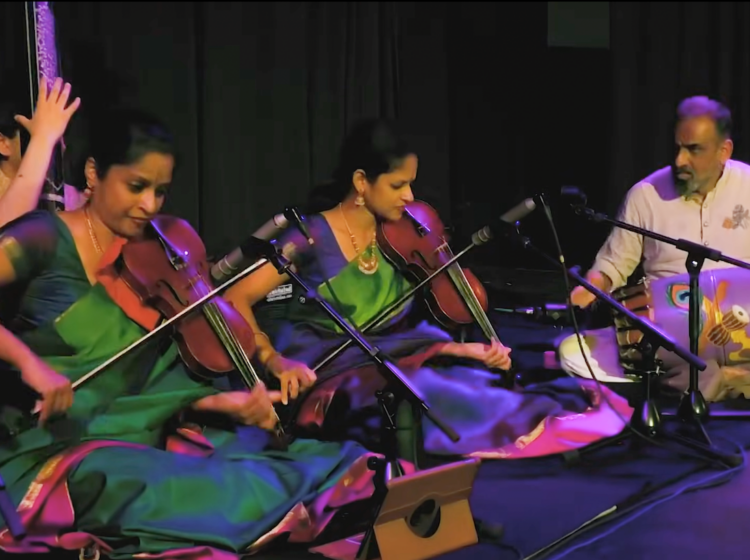 The Akkarai Sisters sitting on stage performing during a concert