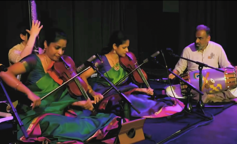 The Akkarai Sisters sitting on stage performing during a concert