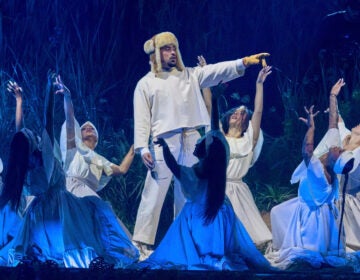 Artist Bad Bunny performs on stage, pointing to something in the distance while dancers surround him