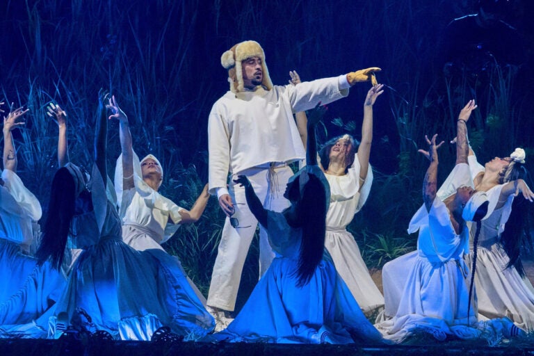 Artist Bad Bunny performs on stage, pointing to something in the distance while dancers surround him