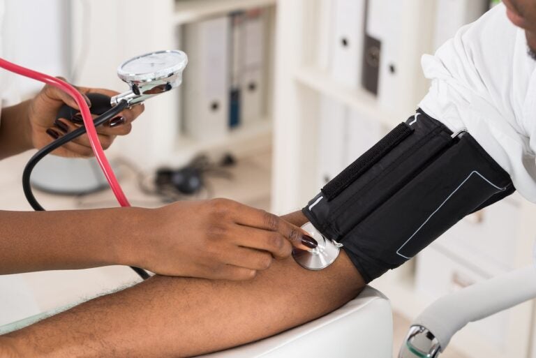 A physician measures a patient's blood pressure with a stethoscope.