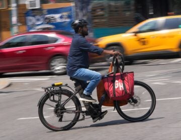 A delivery worker rides a motorized bicycle