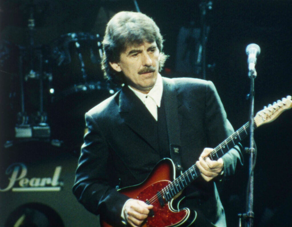 George Harrison performs at a concert, playing guitar on stage