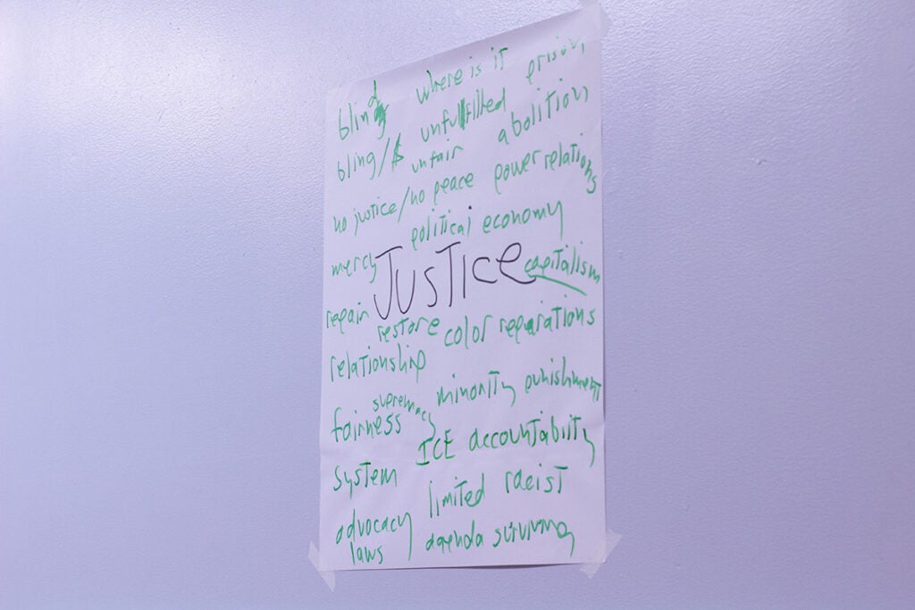 JUSTICE written on a piece of paper on a wall, with other words surrounding it