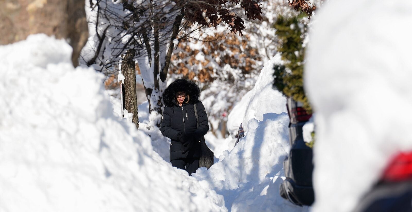 A woman navigates around piles of shoveled snow as she makes her way down a sidewalk, Tuesday, Feb. 24, 2026, in Weekhawken, N.J.