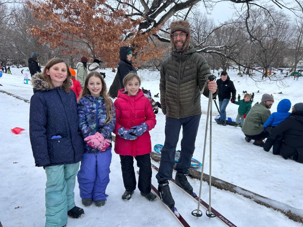 A man on skis poses for a question with three young girls in the park during the snow day