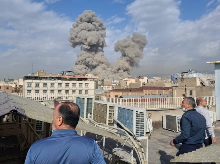 People watch as smoke rises on the skyline after an explosion in Tehran, Iran