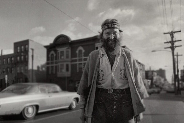Black and white photo of Isaiah Zagar standing on a busy street corner