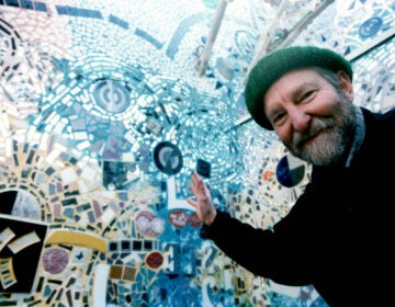 zagar-2026-02-19-Isaiah in PMG Courtyard_ late 90s Isaiah Zagar waving to the camera in the courtyard at the magic gardens