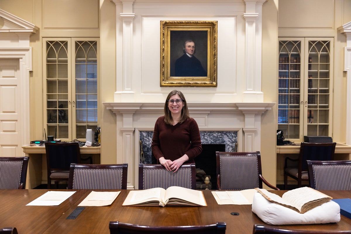Adrianna Link poses inside the Library behind a long table with books and papers on it