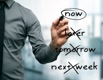 A man crosses out the words later, tomorrow and next week. He circles the word, now.