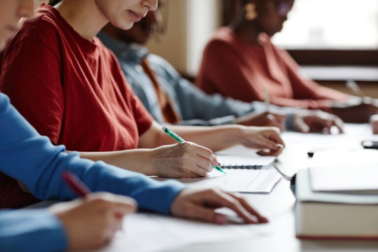 Side view close up of students in row taking notes during lecture in college classroom