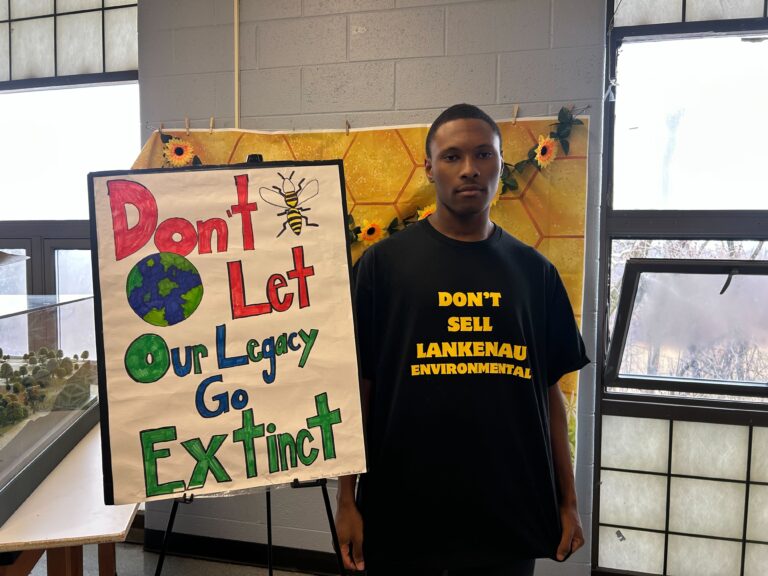 Messiah Stokes next to a sign reading Don't Let Our Legacy Go Extinct