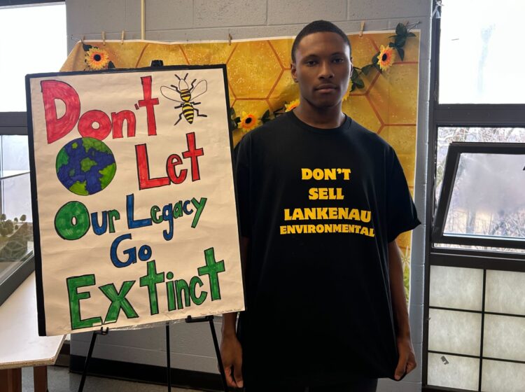 Messiah Stokes next to a sign reading Don't Let Our Legacy Go Extinct
