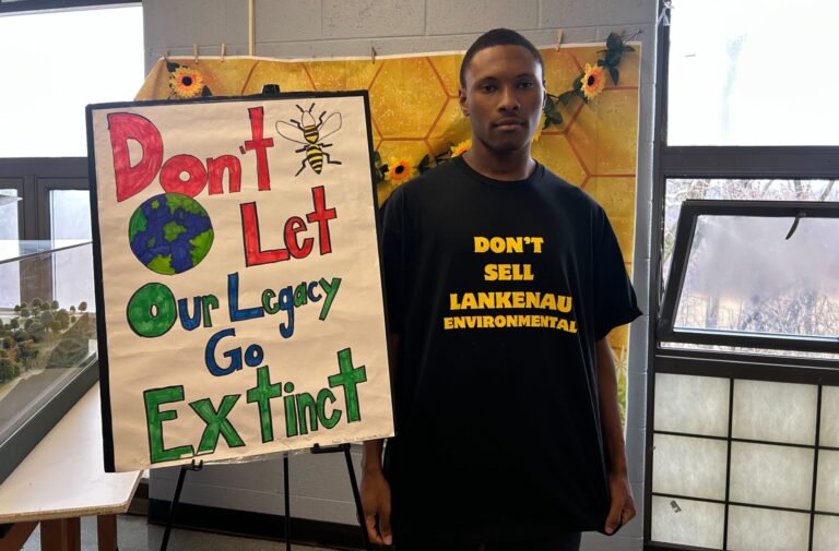 Messiah Stokes next to a sign reading Don't Let Our Legacy Go Extinct