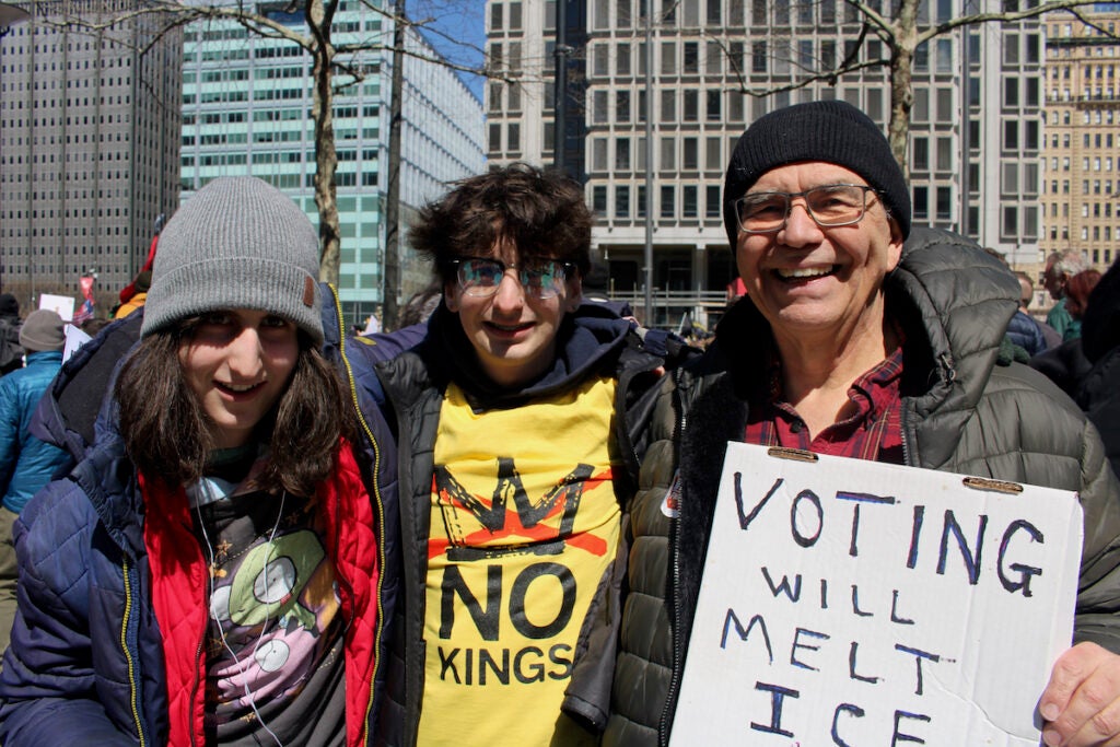 A man, woman and their grandfather pose for a photo while hold signs in Philadelphia protesting the Trump administration.