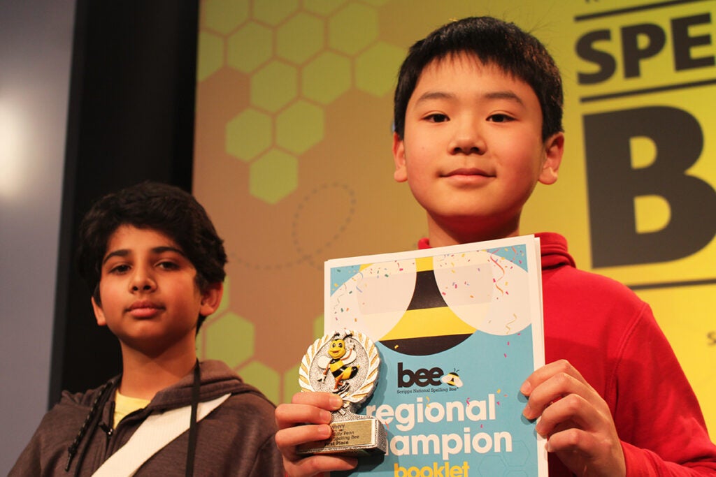 Jayden Jiang, a sixth grader at Girard Academic Music Program, holds up a sign showing he won the WHYY-Billy Penn Philadelphia Regional Spelling Bee, with second place finisher Vidur Diwakar behind him
