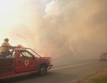 Firefighters drive towards a fire as smoke fills the air.
