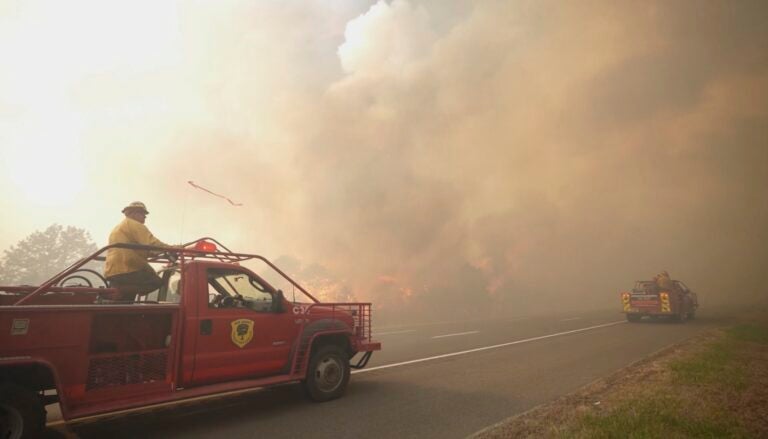 Firefighters drive towards a fire as smoke fills the air.