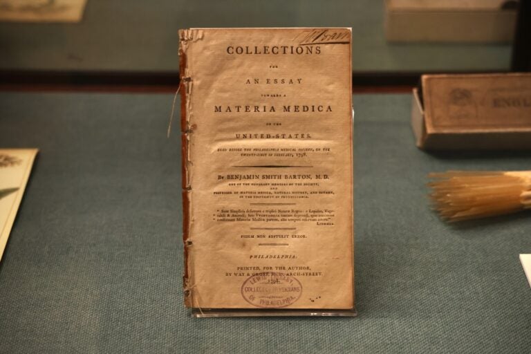 An archival printed book of 'Materia Medica' is on display in a case