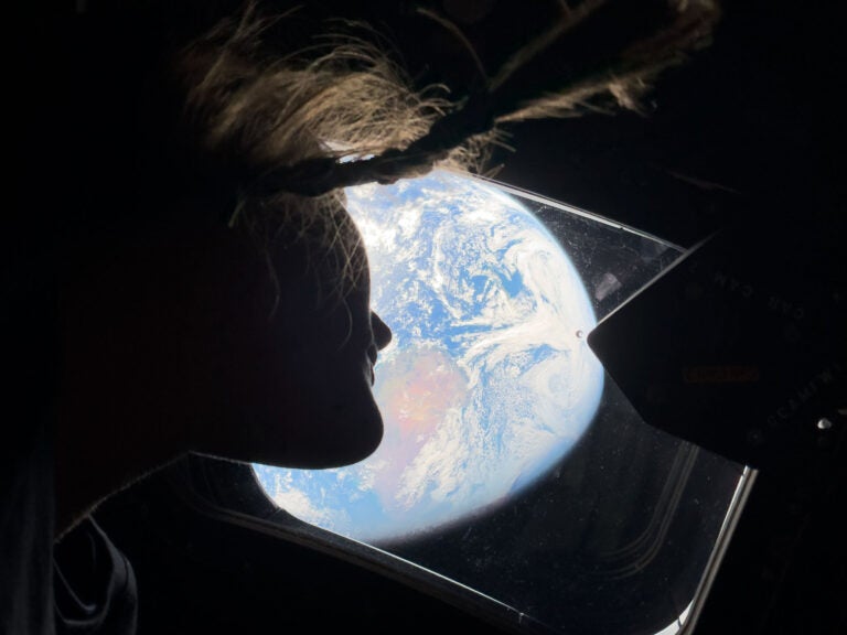 This image provided by NASA, astronaut and Artemis II mission specialist Christina Koch peers out of one of the Orion spacecraft's main cabin windows, looking back at Earth, as the crew travels towards the Moon on Thursday, April 2, 2026.  (NASA via AP)