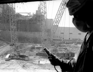 In this 1986 photo, a Chernobyl nuclear power plant worker holding a dosimeter to measure radiation level is seen against the background of a sarcophagus under construction over the 4th destroyed reactor, Ukraine.