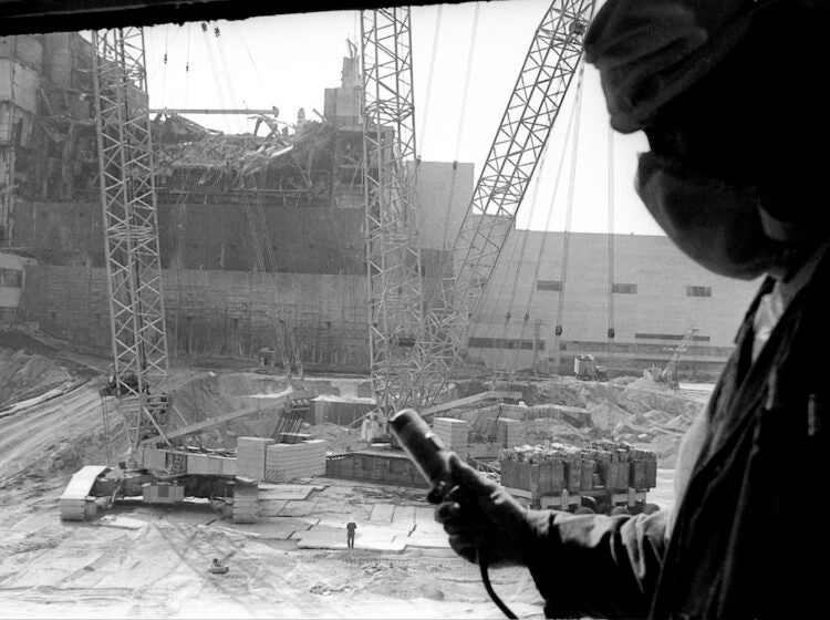 In this 1986 photo, a Chernobyl nuclear power plant worker holding a dosimeter to measure radiation level is seen against the background of a sarcophagus under construction over the 4th destroyed reactor, Ukraine.
